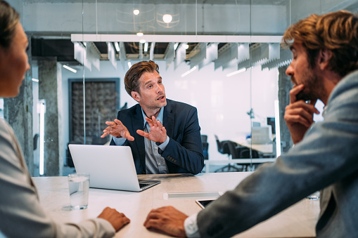 Shot of young couple having a consultation with a financial advisor in the office. Group of business persons in business meeting. Three entrepreneurs on meeting in board room. Corporate business team on meeting in modern office. Male manager discussing new project with his colleagues. Company owner on a meeting with two of his employees in his office.