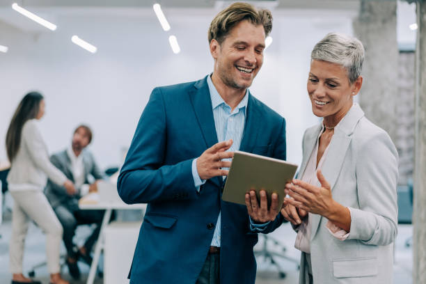 Business people in the office. Shot of two coworkers having a discussion in modern office. Businessman and businesswoman in meeting using digital tablet and discussing business strategy. Confident business people working together in the office. Corporate business persons discussing new project and sharing ideas in the workplace. business caucasian meeting men stock pictures, royalty-free photos & images