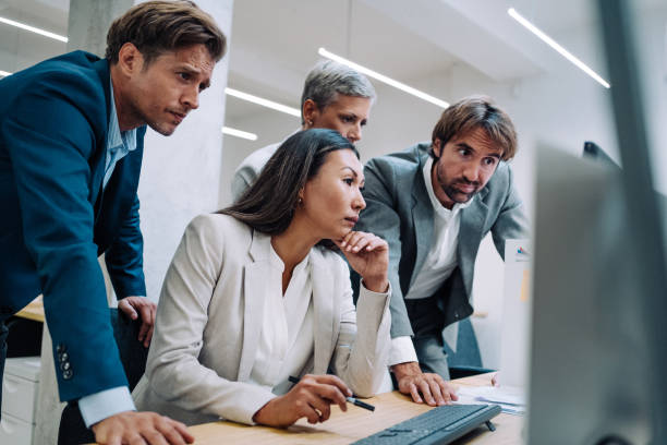 Corporate business people working together in office Shot of a group of colleagues using computer together at work. Four coworkers working on a computer in the office. Multi-ethnic corporate team using computer in modern office. Serious business people cooperating while working on PC. crisis stock pictures, royalty-free photos & images