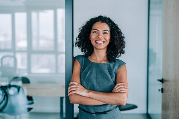 Portrait of a smiling young businesswoman. Portrait of beautiful confident smiling african-american businesswoman standing with arms crossed in the office and looking at camera. portrait power pose stock pictures, royalty-free photos & images