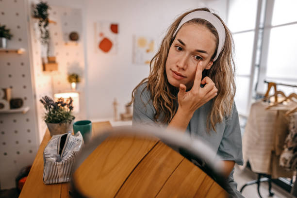 woman rubbing cream under eyes - attractive female indoors lifestyles clean imagens e fotografias de stock