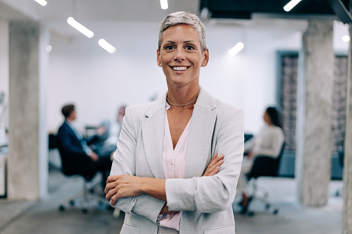 Shot of a beautiful smiling businesswoman standing in front of her team in the office. Portrait of successful businesswoman standing with her colleagues working in background.