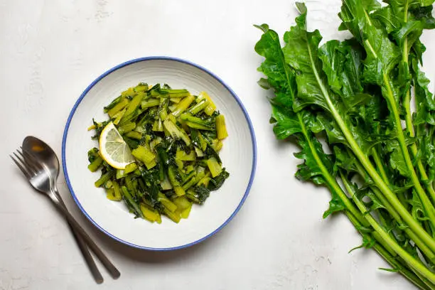 Sauteed chicory greens with olive oil and lemon and fresh head of chicory on white table.