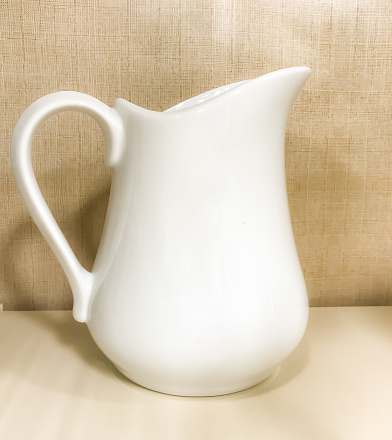 A white porcelain jug, on a wooden base and a black background