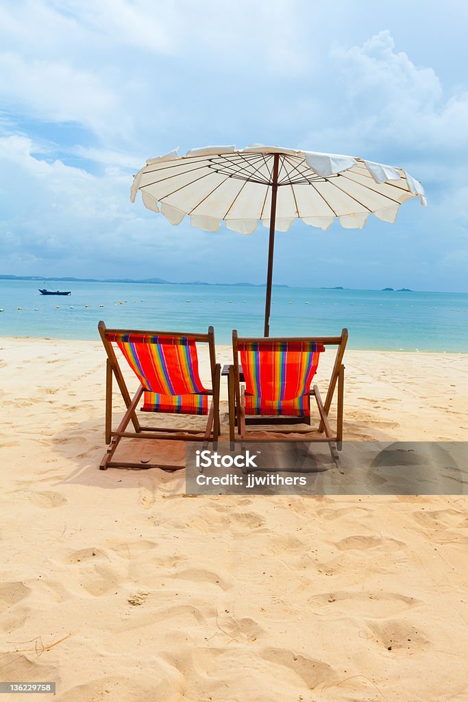 Dos sillas en la arena bajo una sombrilla en la playa - Foto de stock de Silla de jardín libre de derechos