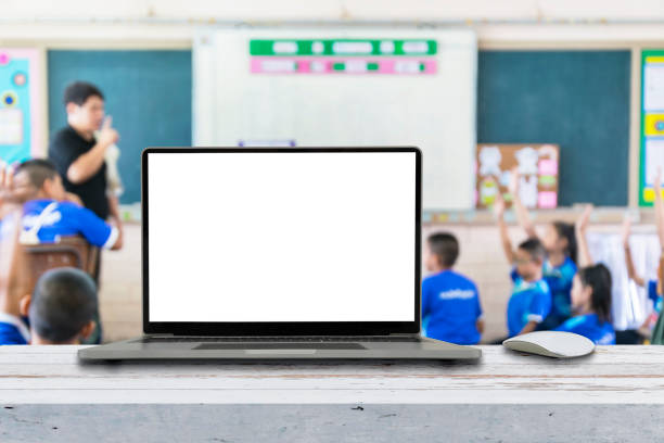 istock Computer on the table, blur image of children in the classroom 1362306396