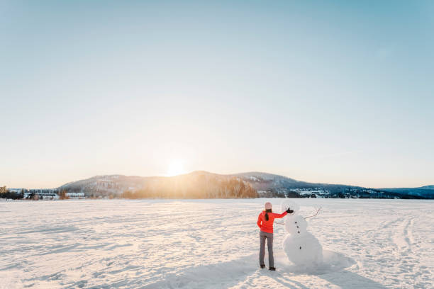 Winter activity. Woman making snowman in winter lake snow nature landscape. stock photo