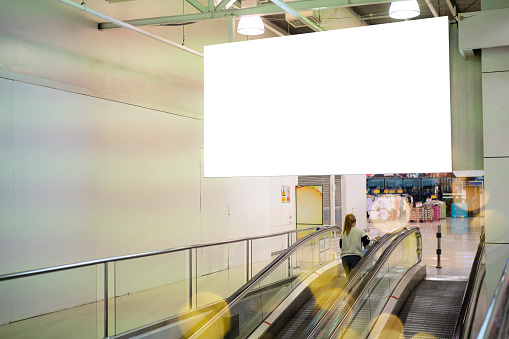 Blank large horizontal poster in public places. A mockup billboard near escalator in airport building, office building or subway station. 3D display.