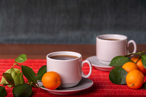 Two cups of coffee with saucers and the tangerines with green leaves on red background. Copy space.