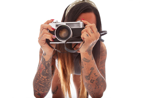 Extreme close-up of a tattooed woman taking a picture with her camera directly at the viewer