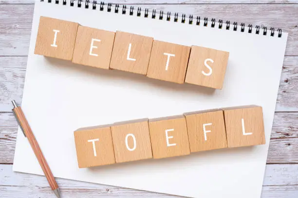 Wooden blocks with "IELTS TOEFL" text of concept, a pen, and a notebook.