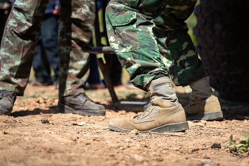 A scene of infantryman or soldier commander is standing on the dust ground with blurred of vehicle part as background, in the war battlefield. Close-up and selective focus at the combat shoe part.