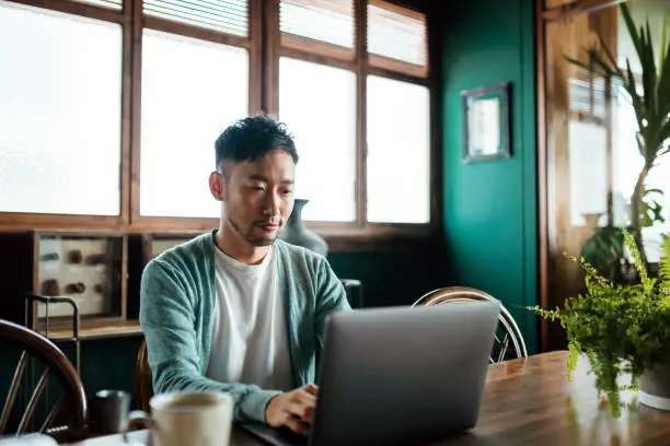 Photo of Professional young Asian man working from home, using laptop computer in home office. Remote working, freelancer, small business concept