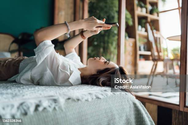 Relaxed Young Asian Woman Shopping Online With Smartphone While Lying In Bed Youth Culture Technology In Everyday Life Stock Photo - Download Image Now