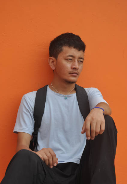 istock An Asian guy looking sideways, sitting against orange wall background with copy space 1362330235
