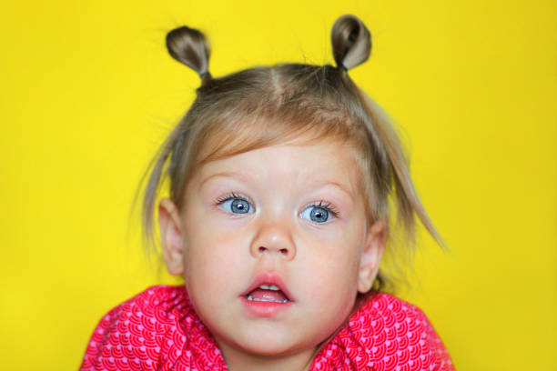 retrato de criança caucasiana intrigada menina de 2 anos com a boca aberta no fundo amarelo - preschool 2 3 years preschooler little girls - fotografias e filmes do acervo