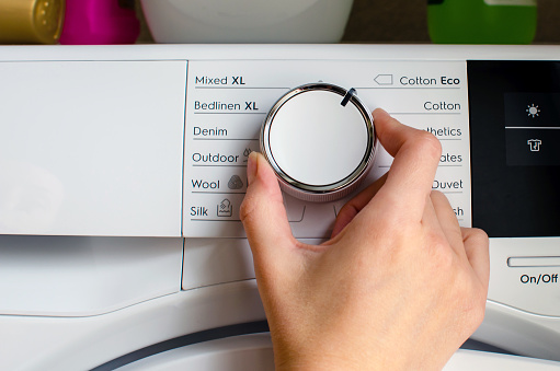 Hand turning the knob of the tumble dryer to adjust the temperature. Dryer setting.