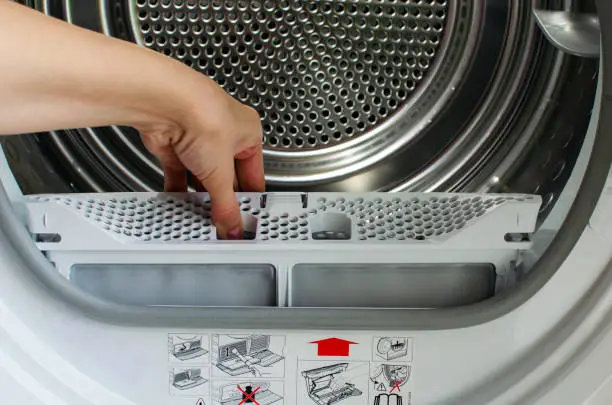 Photo of A housewife holds a lint trap from a front-loading tumble dryer. Woman's hand