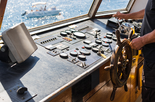 Shot of the hands and arms of an anonymous man who is operating the machinery of a cabin while navigating a ship in the ocean.