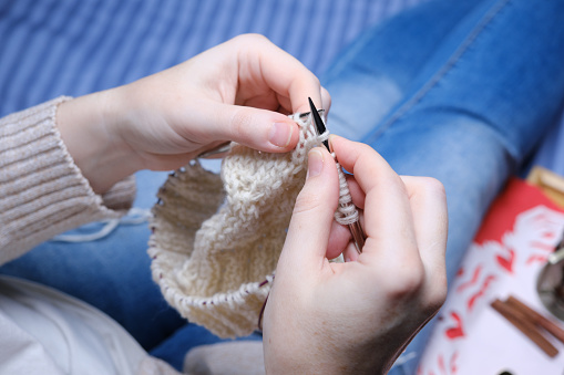 Woman is sitting on the sofa with a cup of tea, a slice of homemade cake and knitting