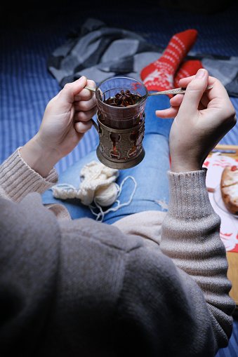 Woman wearing red wool winter socks is sitting on the sofa with a cup of tea, a slice of homemade cake and knitting