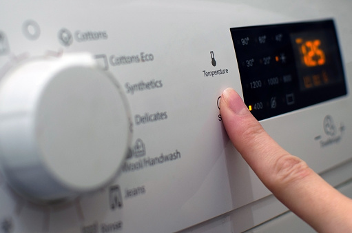 Photo of a woman setting up the washing machine, adjusting the washing parameters, turning on the washing