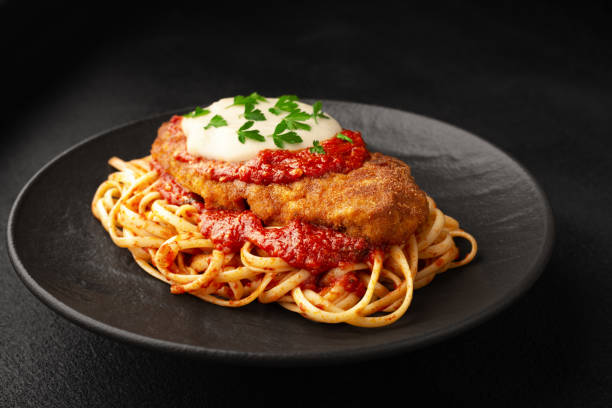 hühnchen-parmigiano mit linguini-pasta auf einem teller mit schwarzem hintergrund - parmesan stock-fotos und bilder