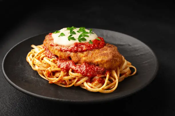 Photo of Chicken parmigiano with linguini pasta on a plate black background