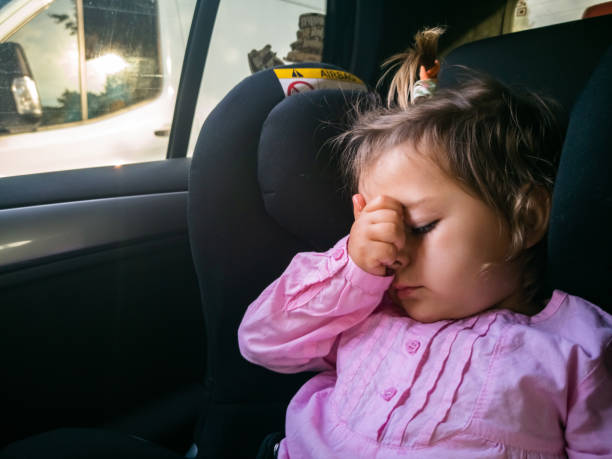 the child was seasick in the car. sad toddler sitting in a child seat stock photo