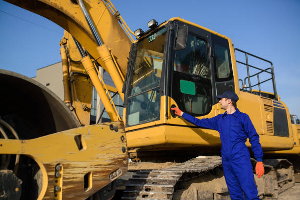 istock Young builder in blue overalls si looking to the excavator 1362346314