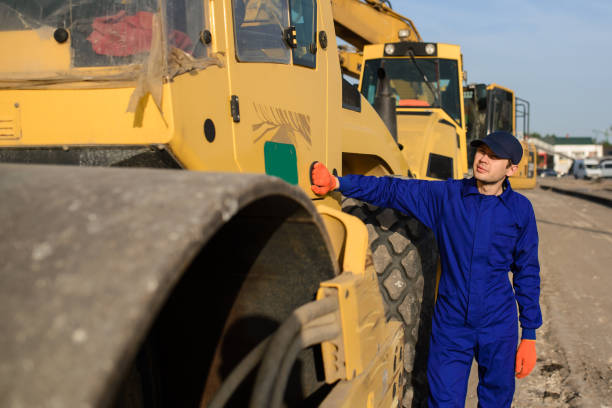 istock Young builder in blue overalls si looking to the excavator 1362346334