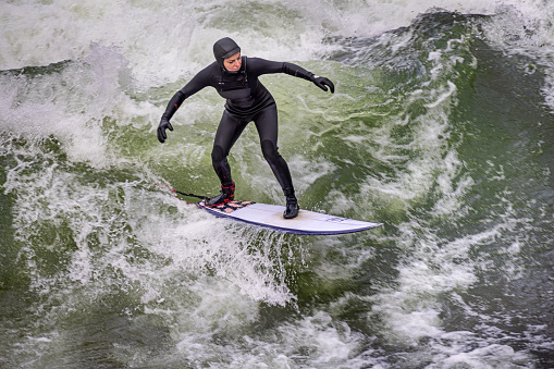 Young man surfing on a river with a continuous wave. The place is called Eisbachwelle and can be found in the middle of the German city Munich.