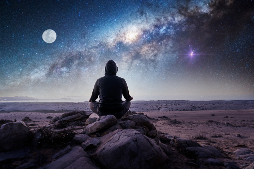 unknown person meditating outdoors at night on top of the mountain with  Milky Way and Moon background