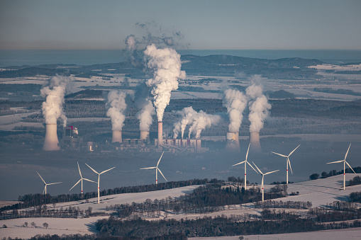 A giant smoking coal-fired power plant near the Czech-Polish border. In the foreground wind turbines producing greener energy.