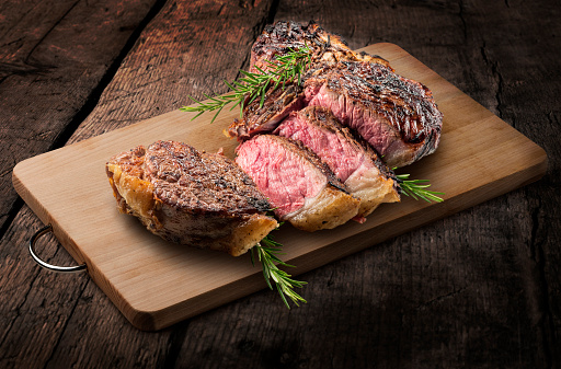 Fiorentina T-bone steak cut and rosemary on rectangular wooden chopping board isolated on wooden background