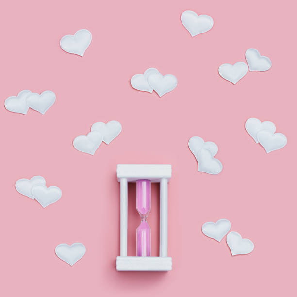 istock Hourglass with pink sand and white hearts around on pink background. 1362364280
