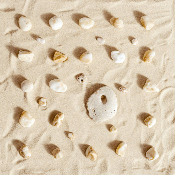 istock Pattern with one big stone with hole and many small on fine sand backgrund. Natural happy stone light ivory color. Symbol of fun, fortunate, lucky. 1362364368