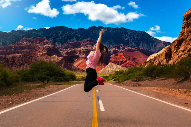 joven saltando en medio de la carretera vacía - turismo argentina fotografías e imágenes de stock