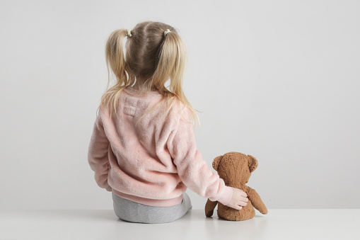 Vista trasera de una niña sentada y abrazando a su oso de peluche photo