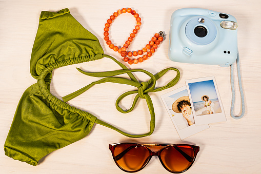 Flat lay beach travel instant camera swimsuit glasses beads