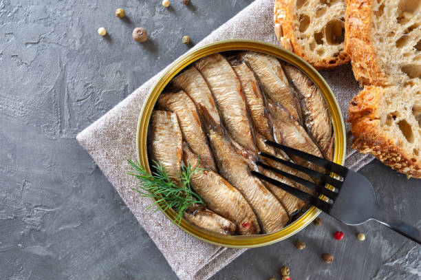 istock Sprats in an open tin can, stacked in rows, prick on a fork. Delicious canned fish serve on crispy bread. 1362369824