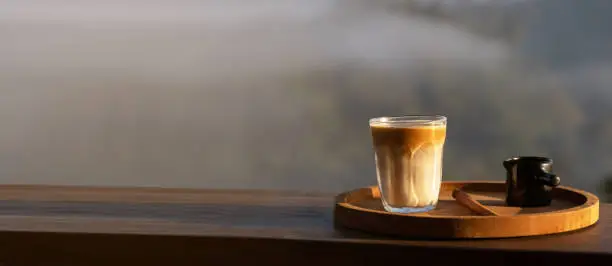 Sunrise coffee in nature. Dirty coffee on wooden table with mountain fog on shade of sunrise background. Good morning.