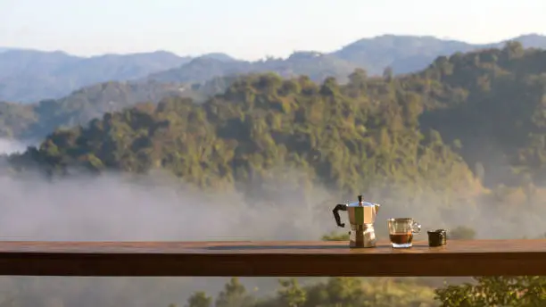 Sunrise coffee in nature. Moka pot with coffee on wooden table with mountain fog on shade of sunrise background. Good morning. 16:9