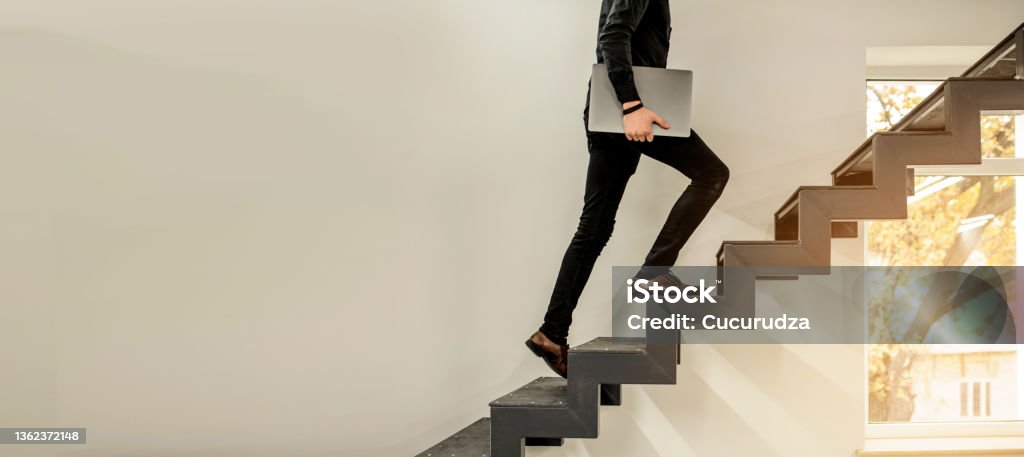 man climbing on a stairs and holding a laptop. Close up of a man climbing on a stairs and holding a laptop. Copy space for your text Staircase Stock Photo