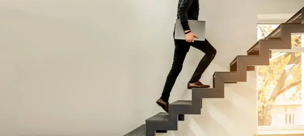 Close up of a man climbing on a stairs and holding a laptop. Copy space for your text