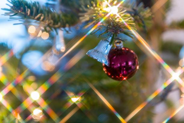 Red colored Christmas ball with a silver Christmas bell and star shaped lights in a Christmas tree.
