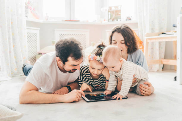 Family with two daughter using tablet, laptop for playing game watching movies, relaxing at home for lifestyle concept Family with two daughter using tablet, laptop for playing game watching movies, relaxing at home for lifestyle concept 6 9 months stock pictures, royalty-free photos & images