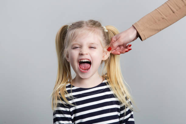 непослушную маленькую девочку наказывают вытягиванием ушей, студийный выстрел - crying grimacing facial expression human face стоковые фото и изображения