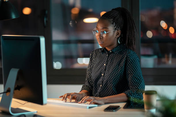 donna imprenditrice piuttosto felice che lavora con il laptop seduta in ufficio. - african ethnicity women laptop computer foto e immagini stock