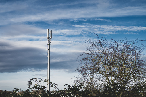 Distant 5G cellular communications tower seen in the English countryside. Also seen is microwave and 3 and 4G telecoms equipment.